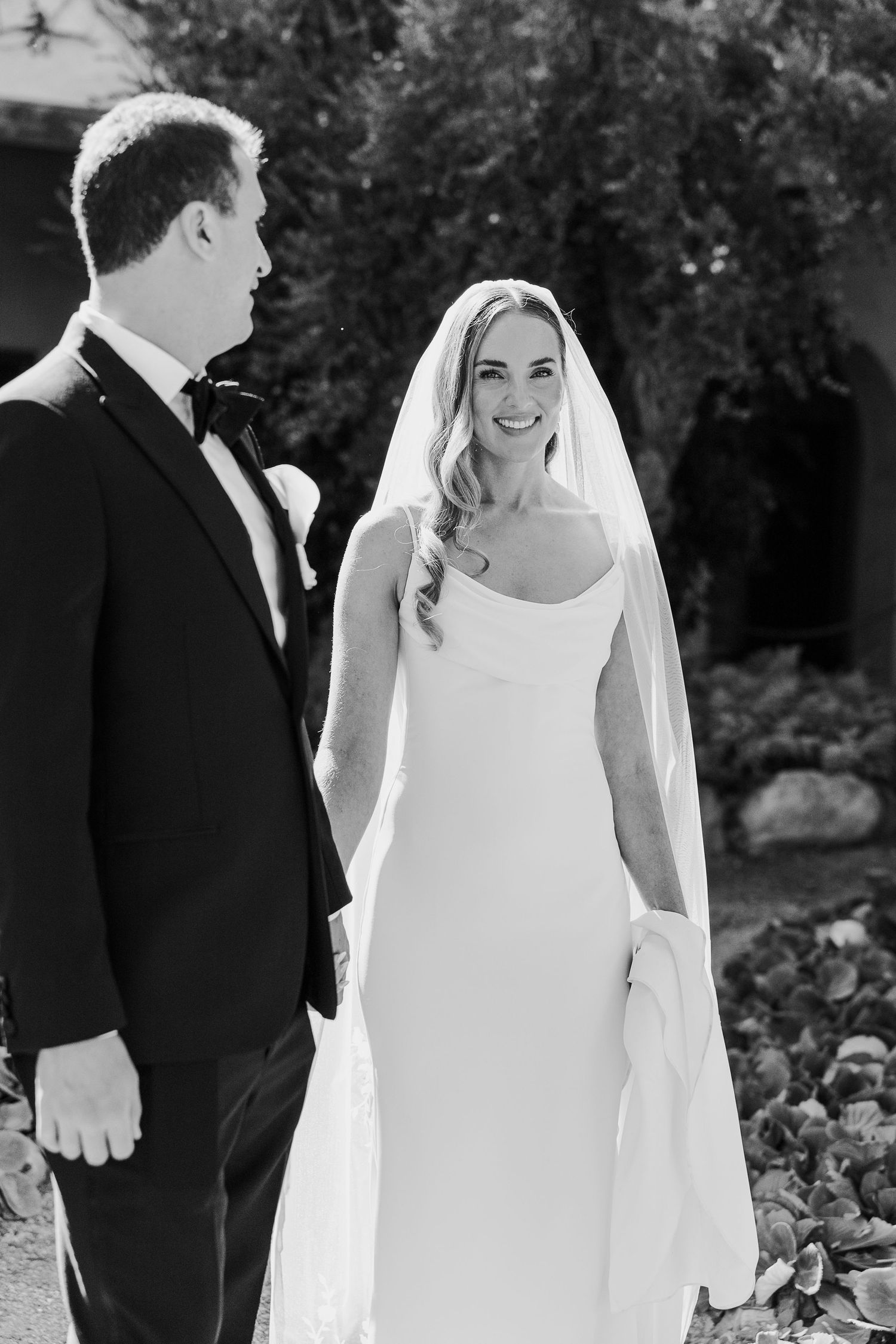 Black and white wedding photos show a bride in sleeveless dress and groom in tuxedo walking together outdoors.