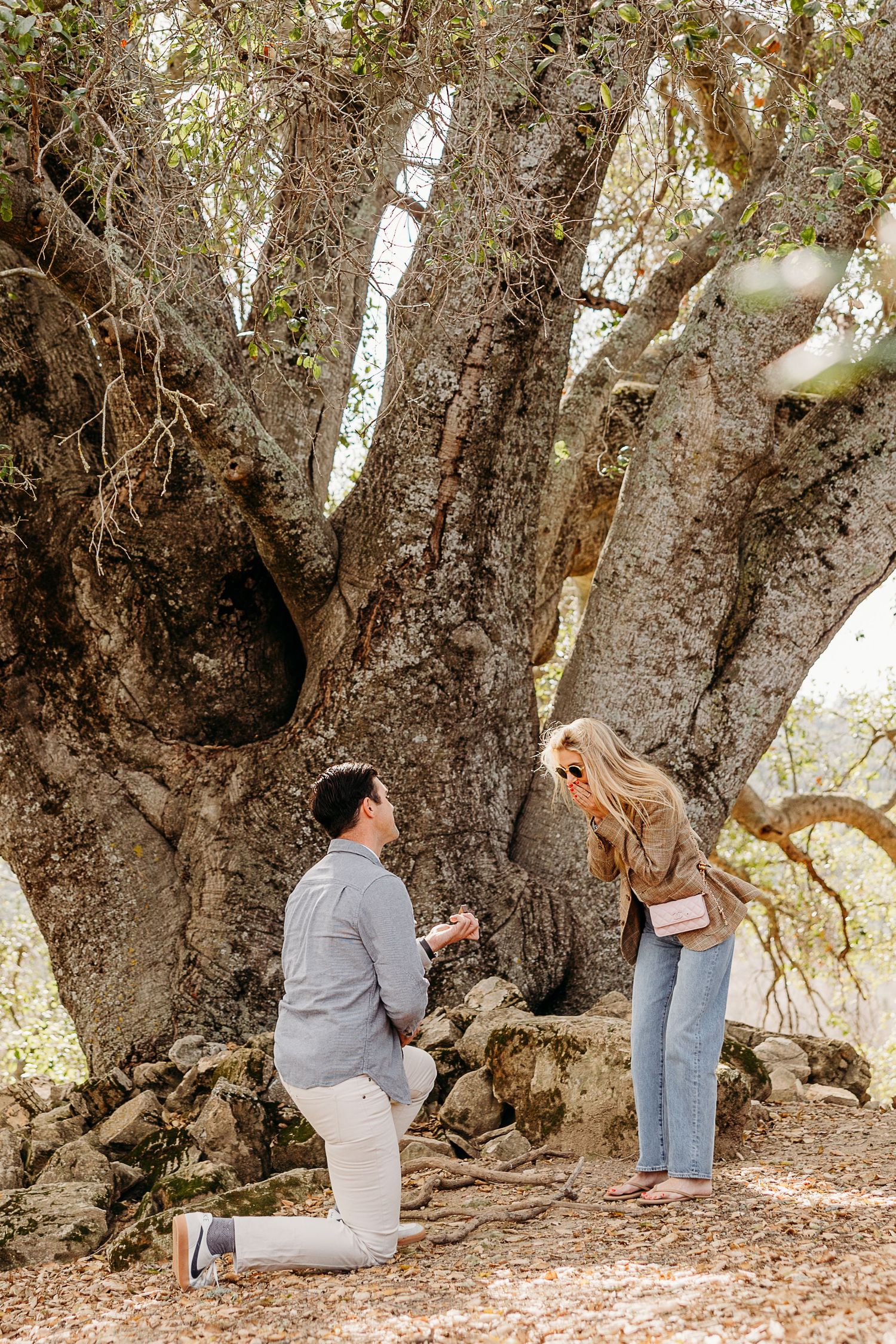 Couple exploring beneath a large gnarled tree trunk in a natural outdoor setting.