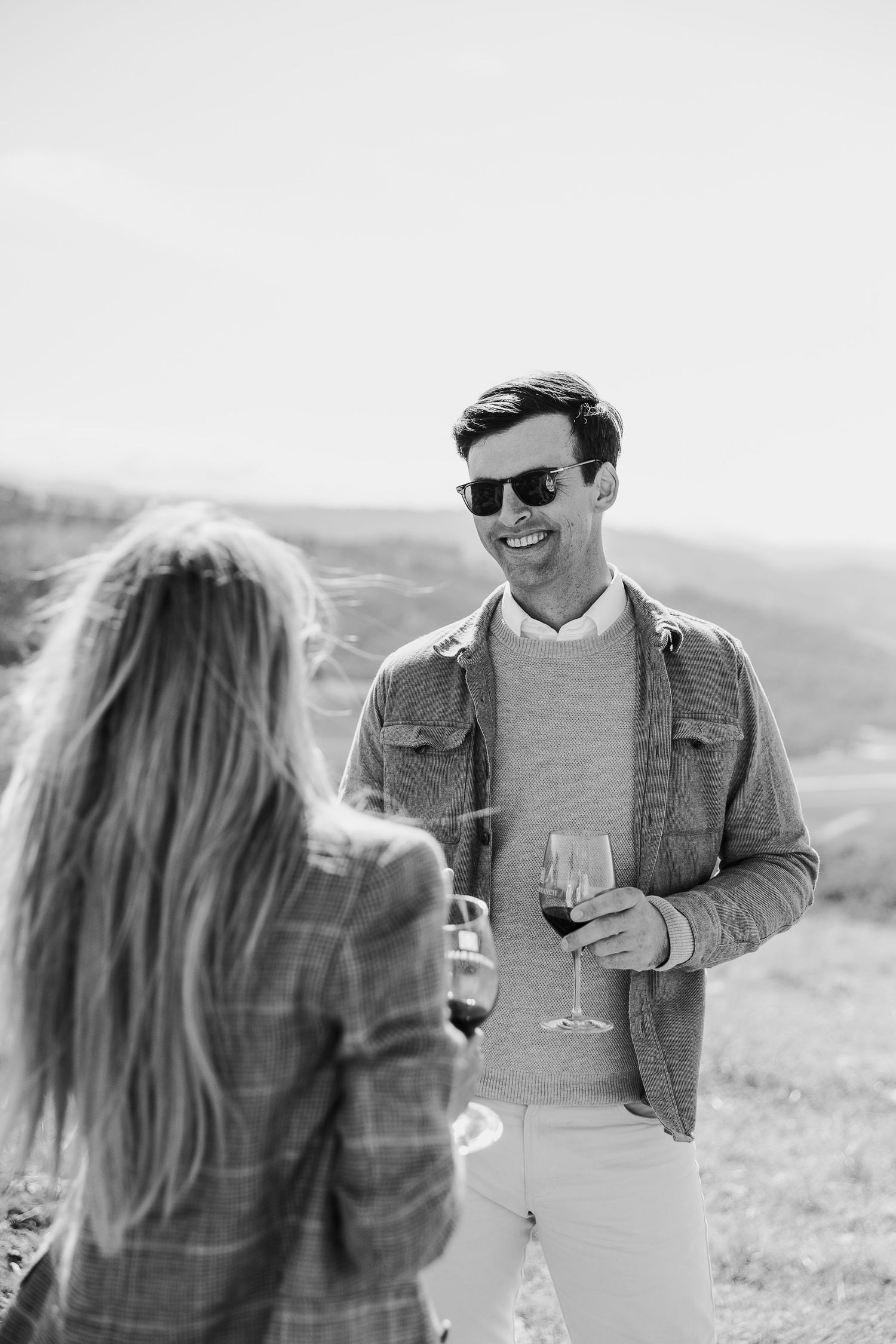 Black and white photo of couple toasting with wine glasses in outdoor setting.