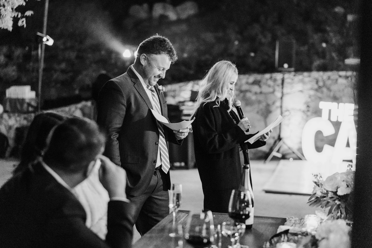 Black and white photo of guests enjoying speeches during an evening wedding reception.