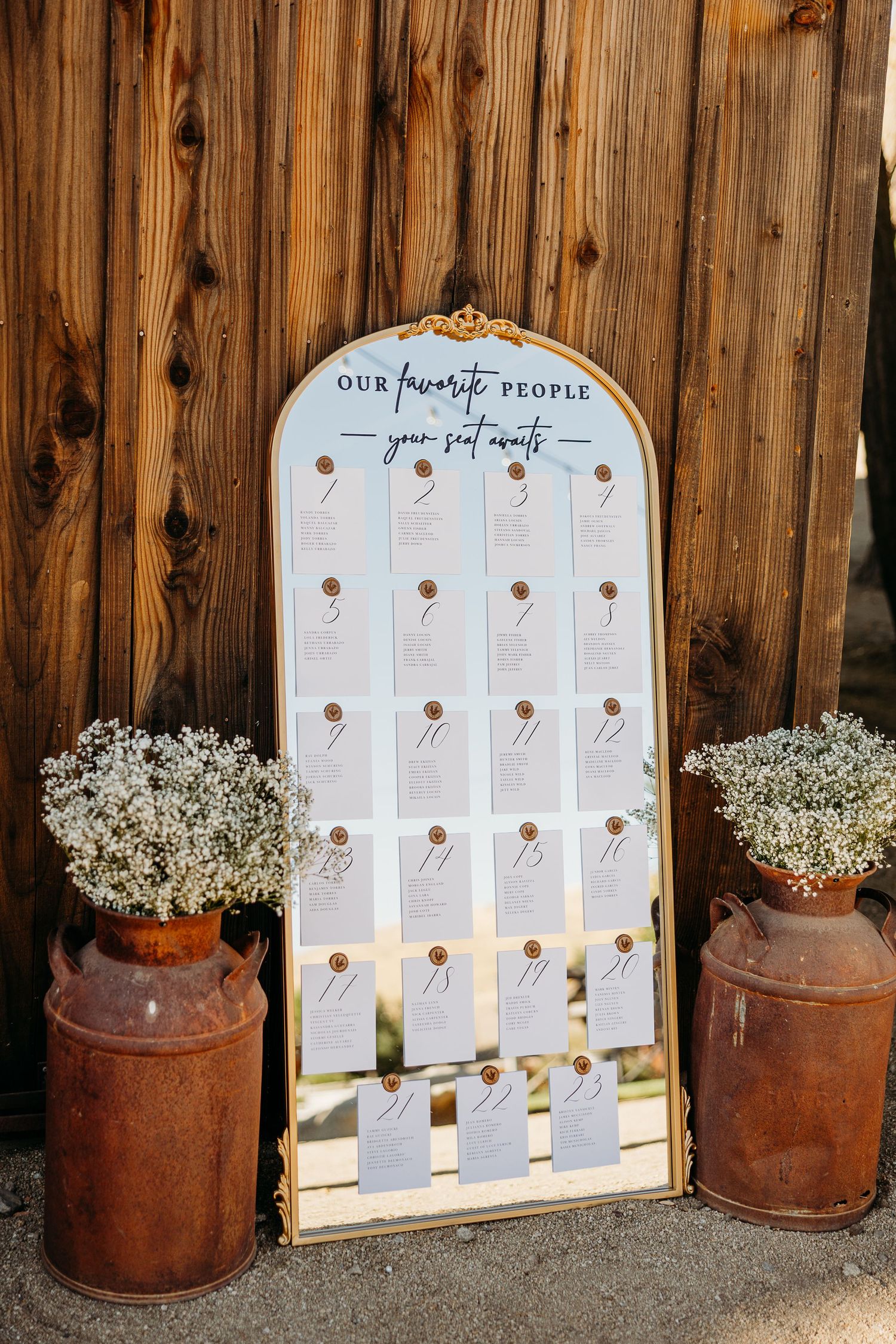 Rustic wedding seating chart display with vintage milk cans and baby's breath flowers against wooden backdrop.