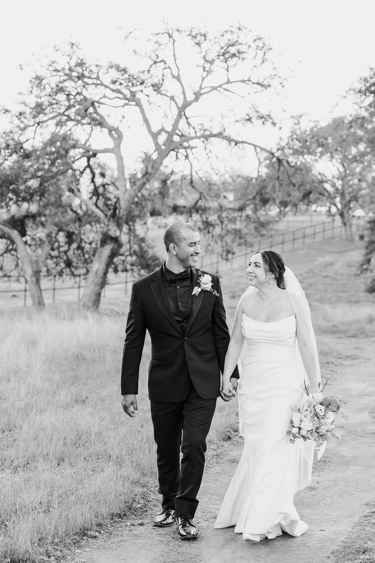 Black and white photo of a couple walking through a scenic field with oak trees.