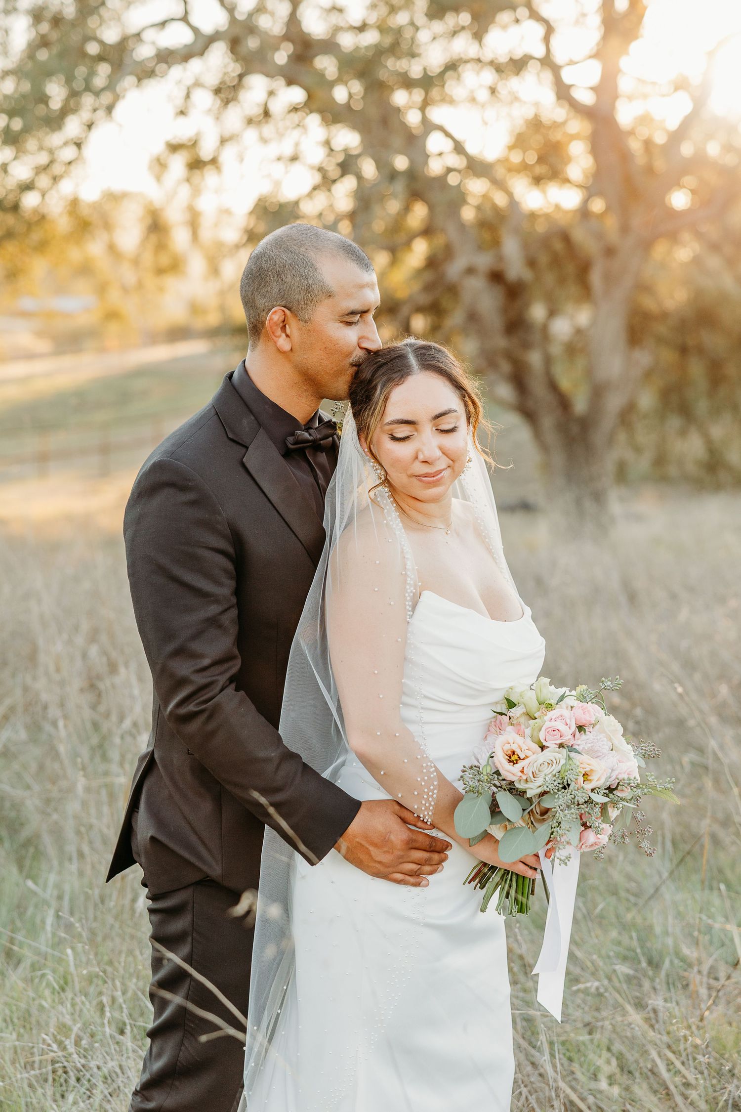 Romantic sunset wedding portrait in a golden field with elegant floral bouquet.