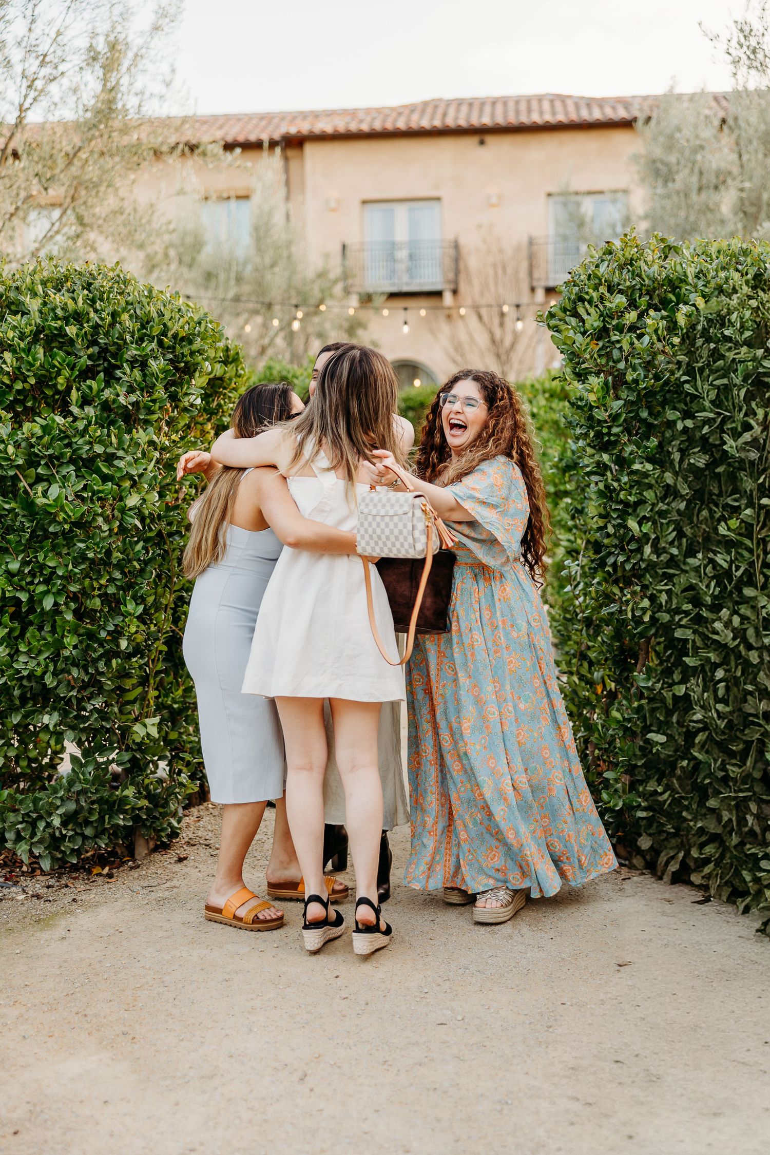 Group of friends walking together along a garden path next to a hedge wall.
