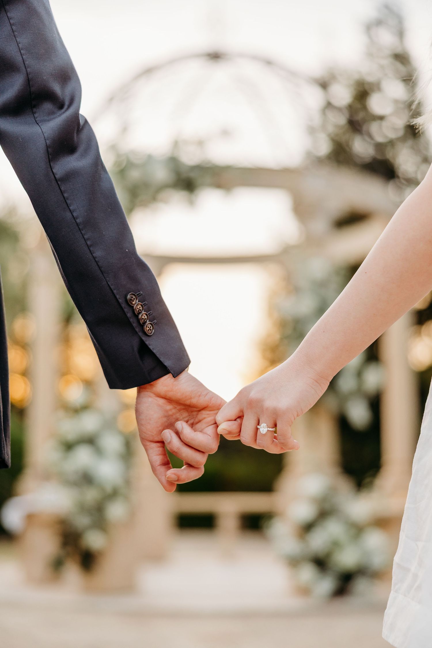 Close-up of hands reaching for each other in a romantic garden setting.