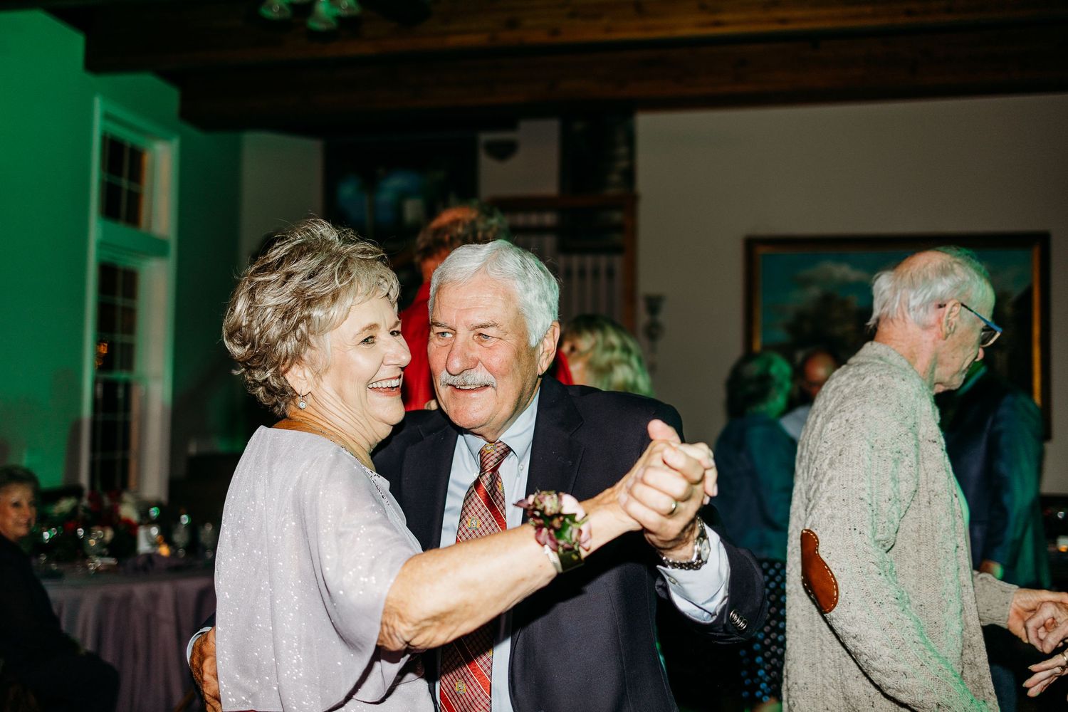 Elderly couple dancing together at evening wedding reception in dimly lit venue.