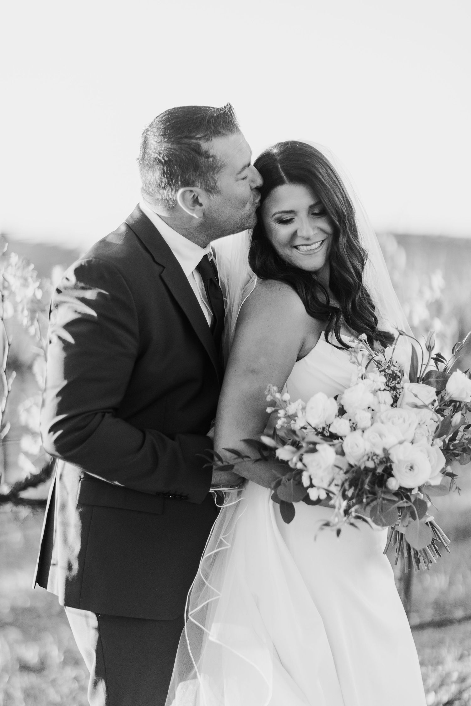 Romantic wedding couple embracing with white floral bouquet against bright background.