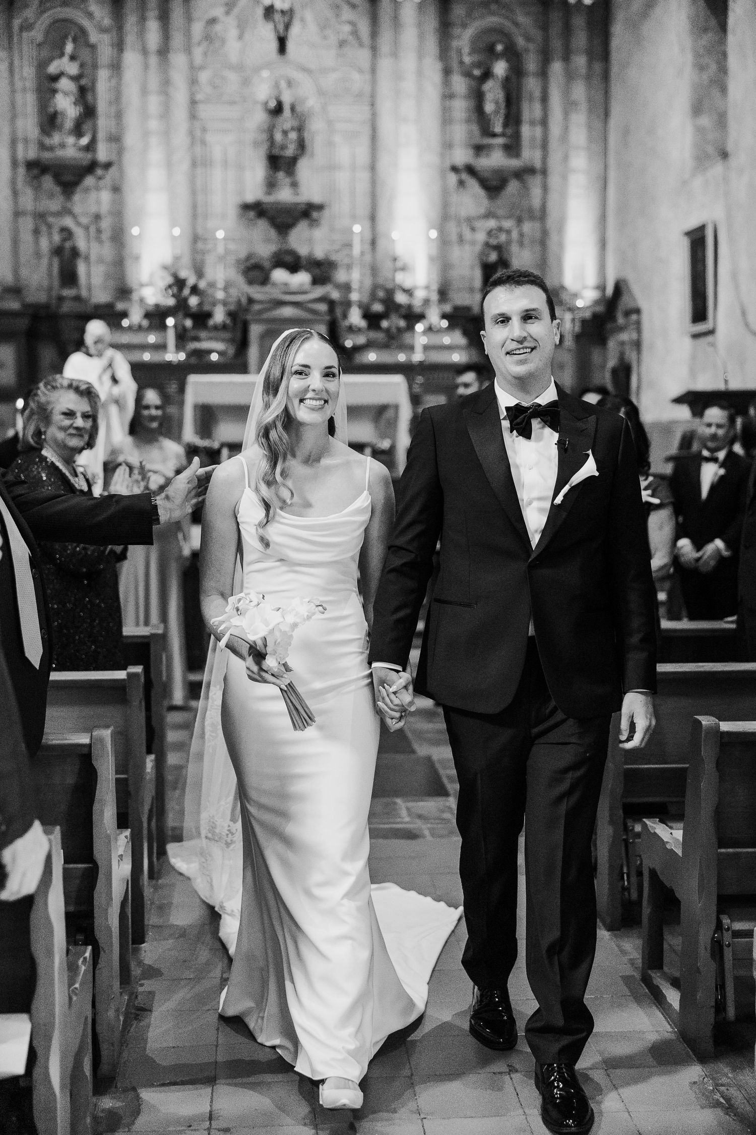 A couple walks down the church aisle after their wedding ceremony in black and white.
