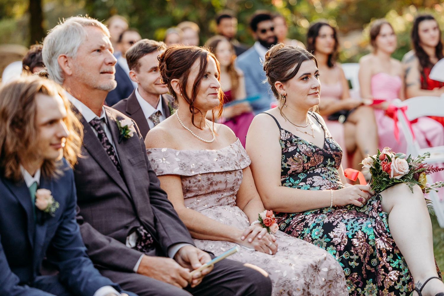 Wedding guests seated outdoors in formal attire with floral decorations.