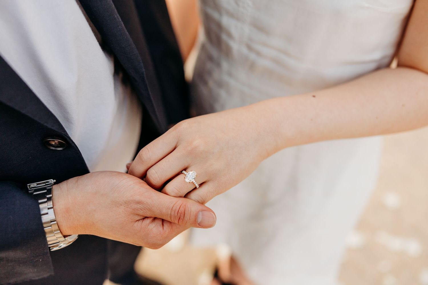 Close-up view of hands with wedding rings resting on a white surface.