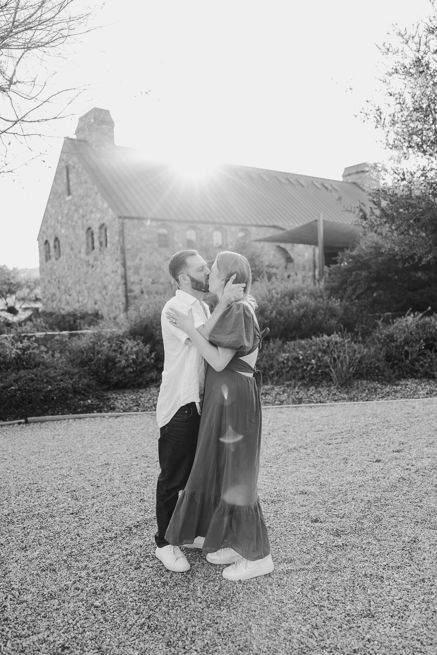 A romantic couple embraces in black and white photography with a stone building in the background.