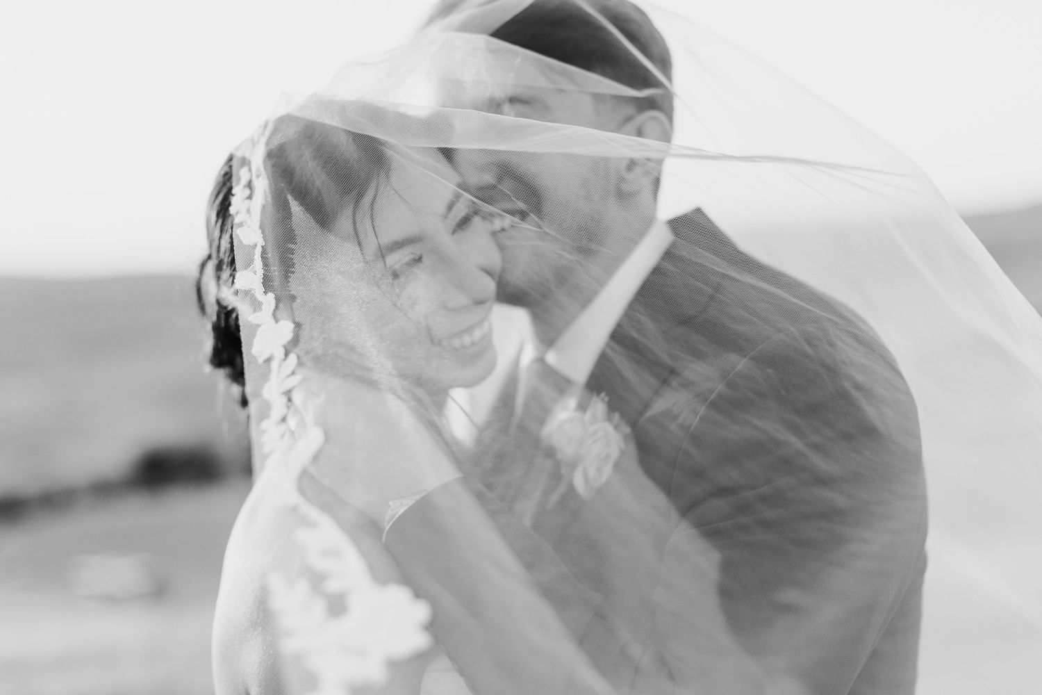 Flowing white wedding veil catches wind against bright sky during outdoor wedding photoshoot.