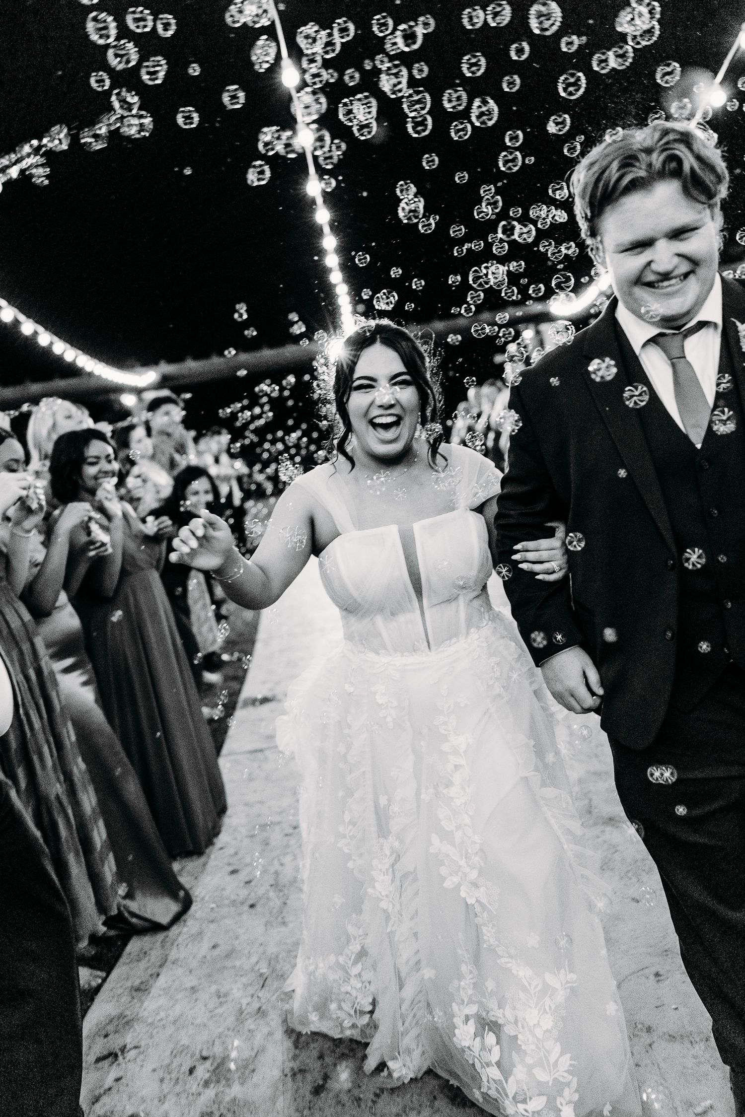 Happy couple walks through shower of bubbles during wedding celebration.