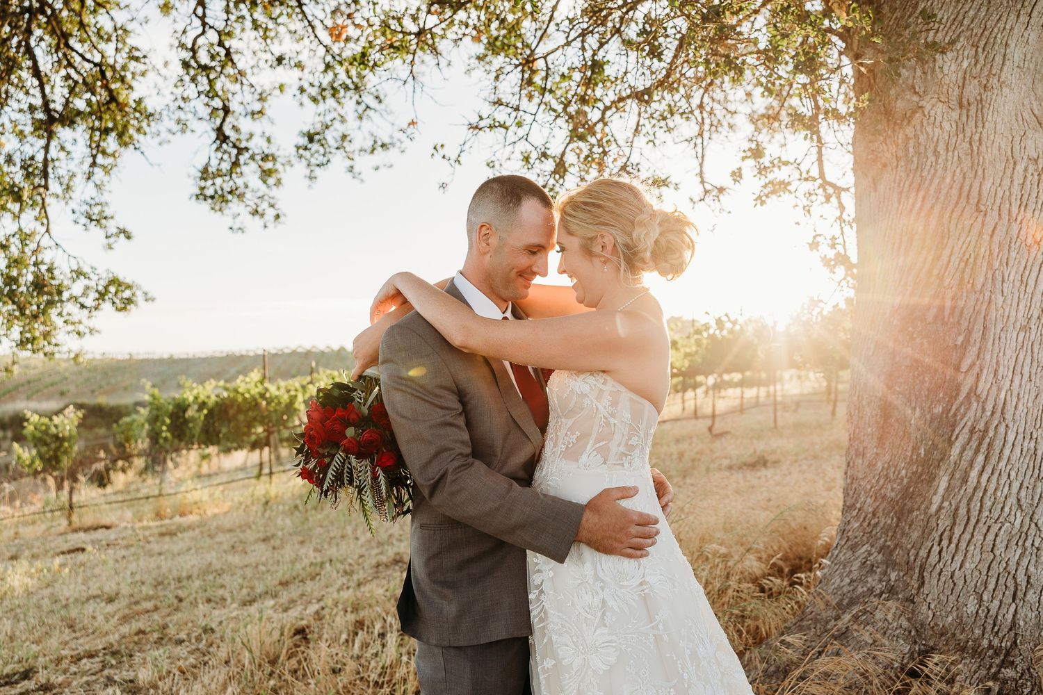 A couple sharing an intimate moment at sunset in a vineyard setting.
