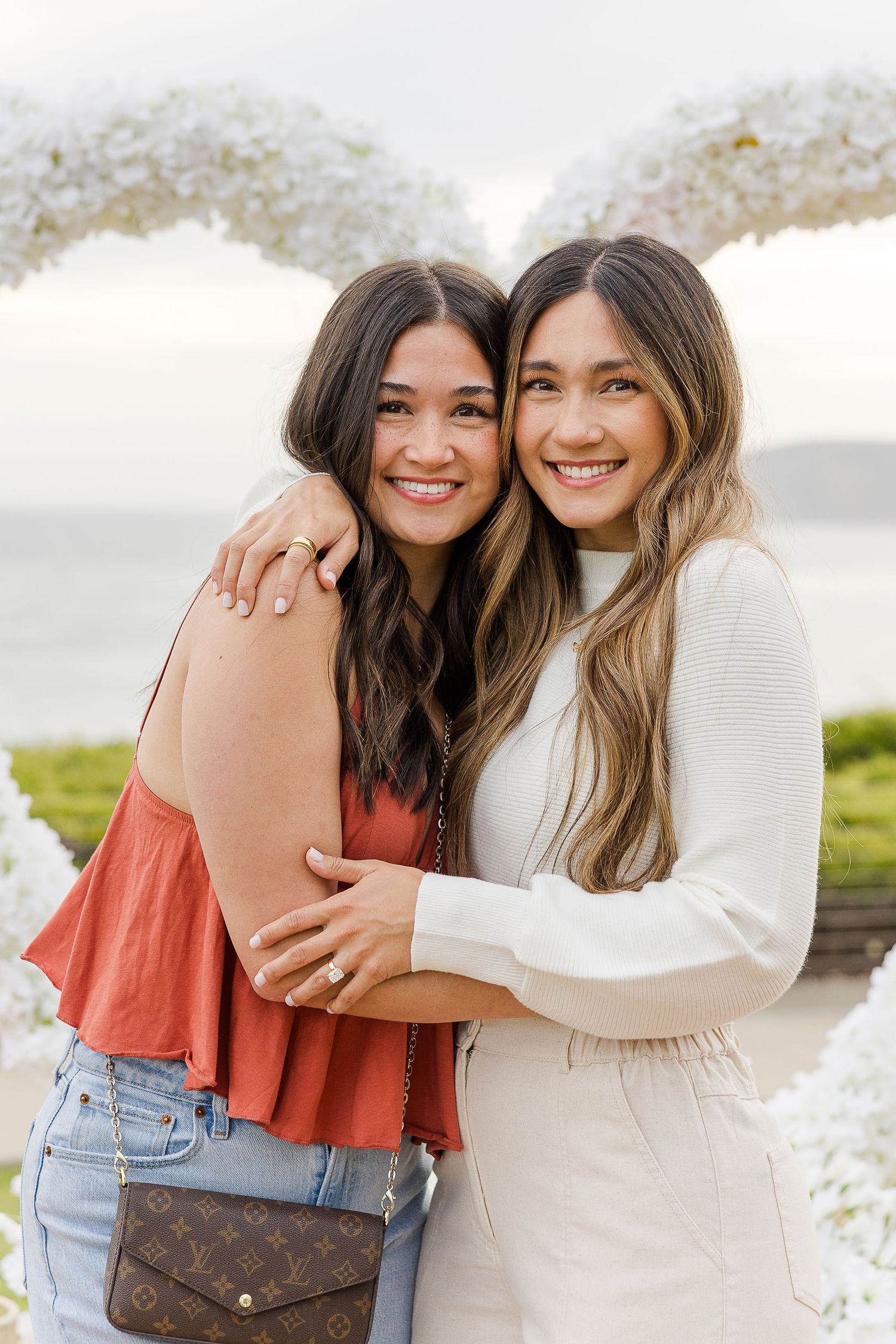Two friends embracing and smiling together outdoors on a sunny day near the water.