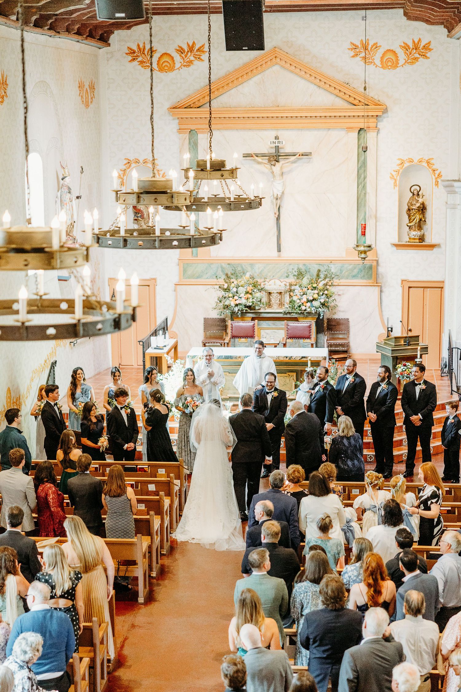Traditional Catholic church wedding ceremony with ornate decorations and full pews of guests watching the service at the altar.