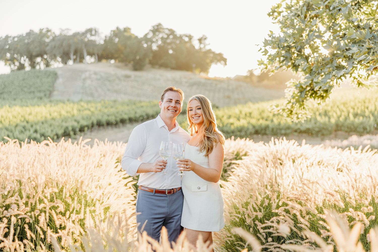Romantic couple embraces in sunlit field during summer evening photoshoot.