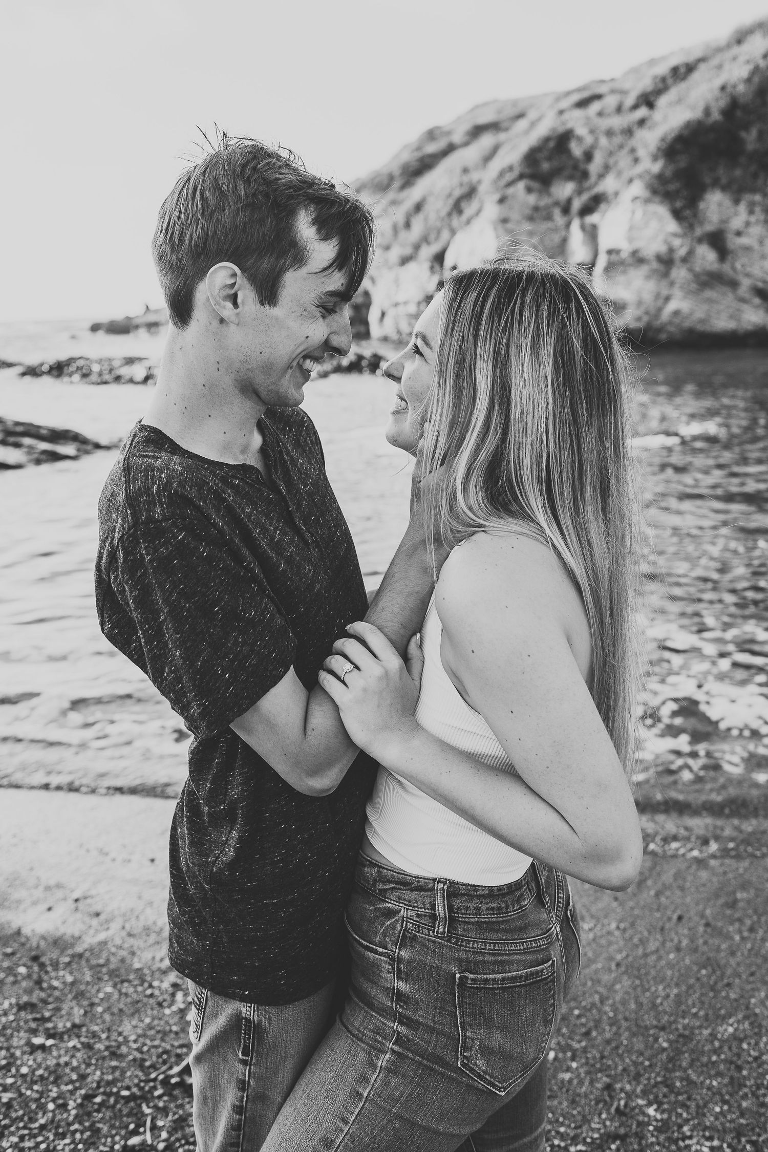 A black and white portrait of a couple sharing a tender moment by the ocean.