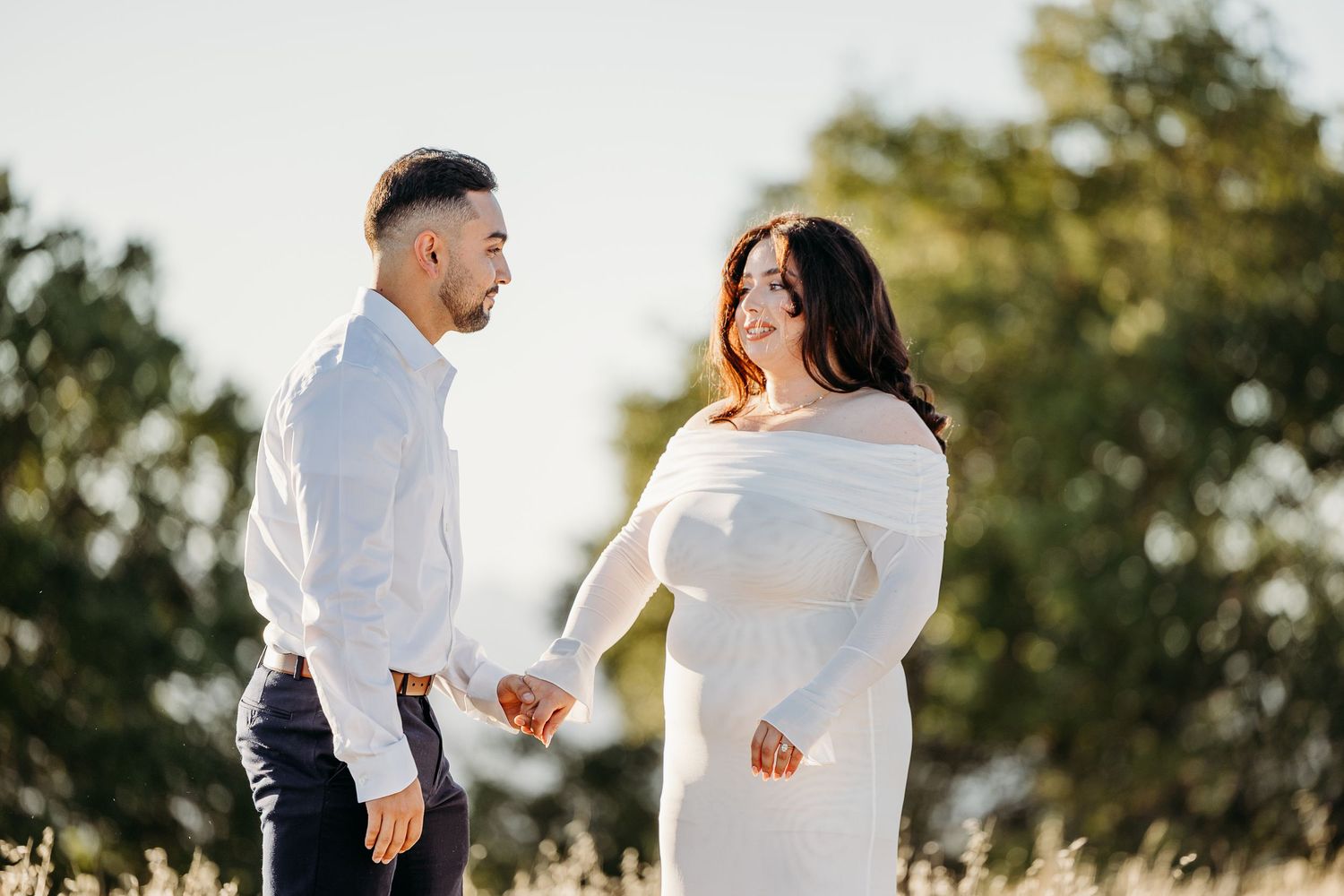 A joyful couple celebrates their engagement outdoors on a sunny afternoon surrounded by trees.