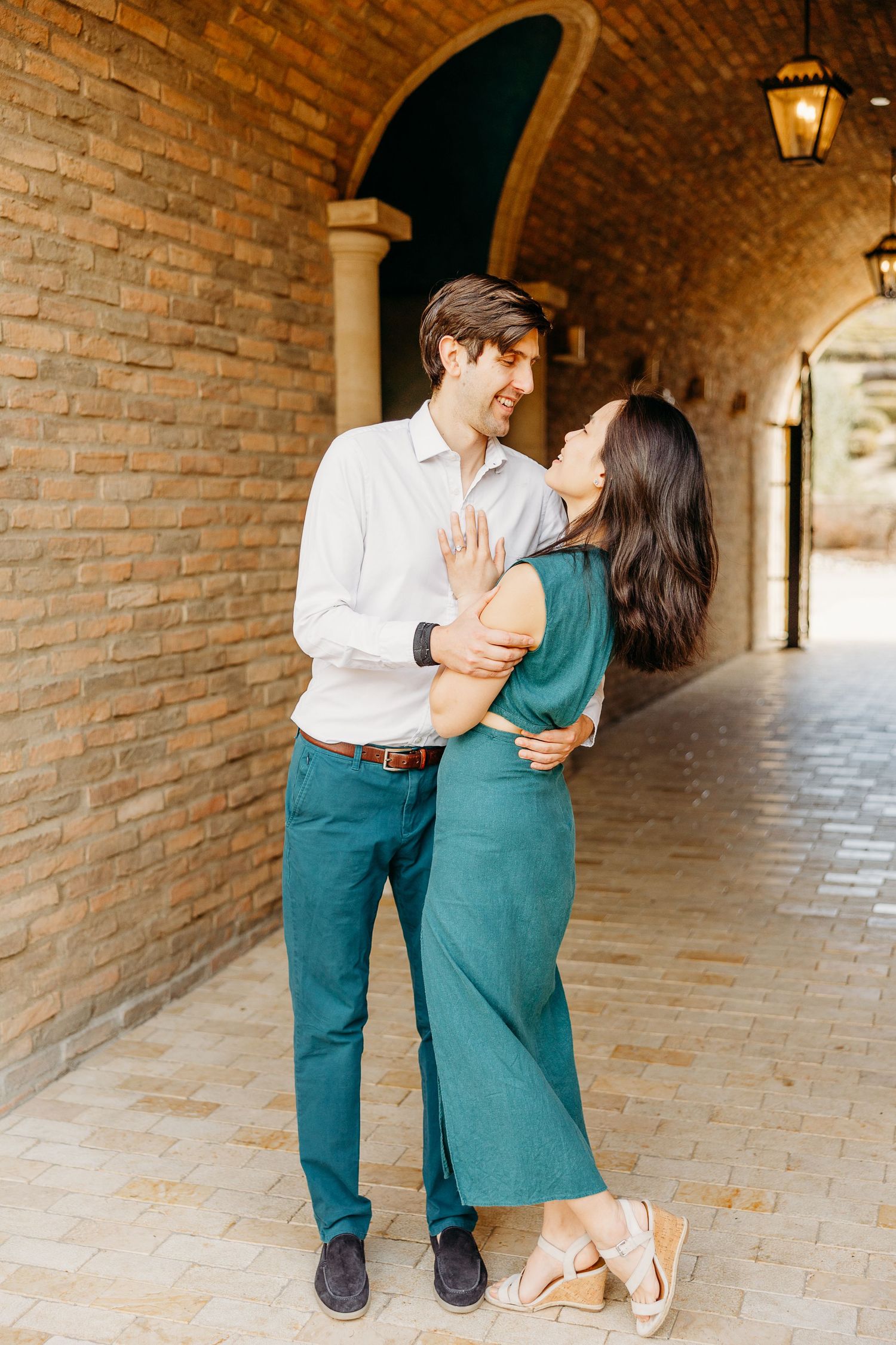 Couple in coordinating outfits share an intimate moment under a brick archway with warm lighting.