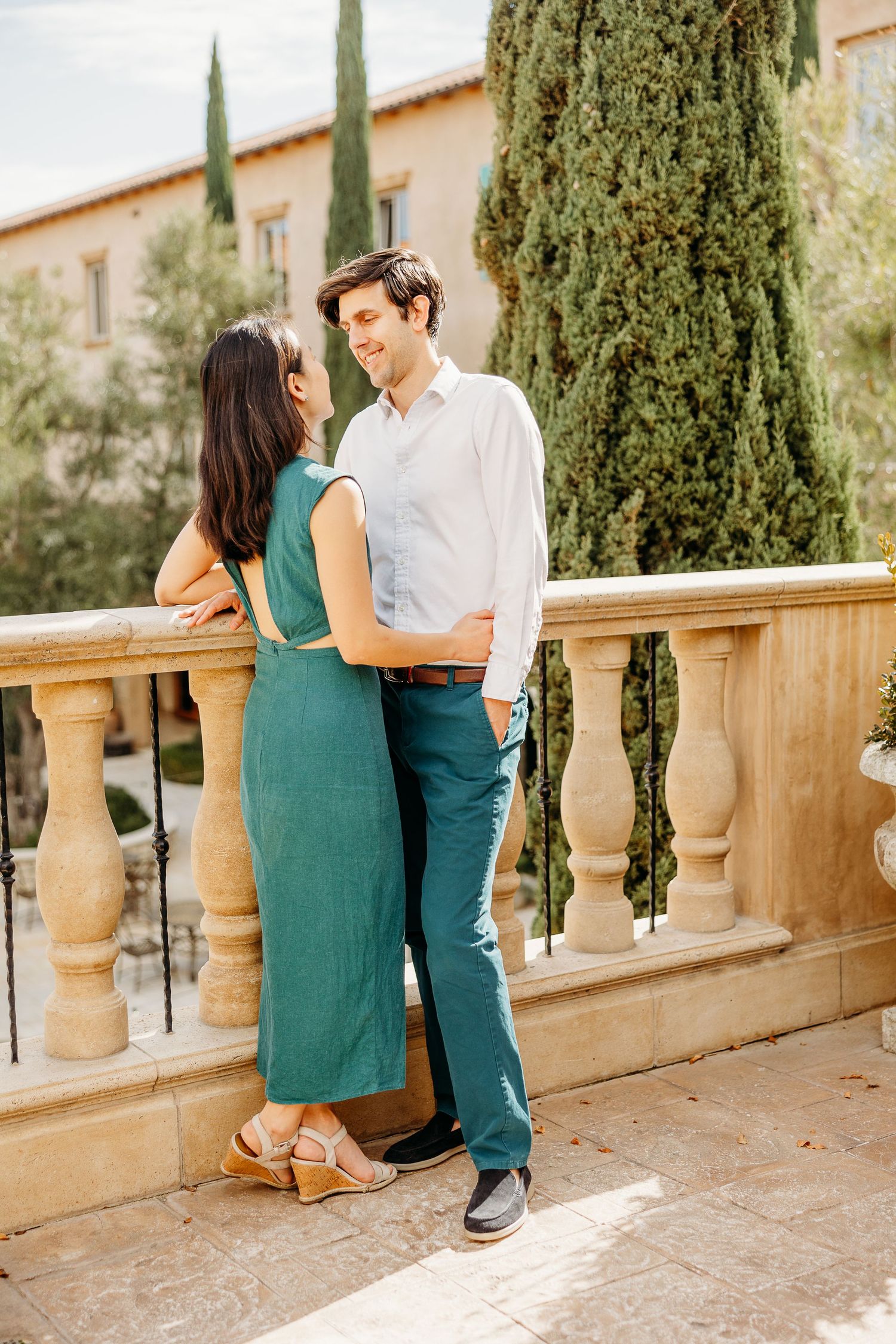 Couple sharing an intimate moment on a Mediterranean style balcony with cypress trees.