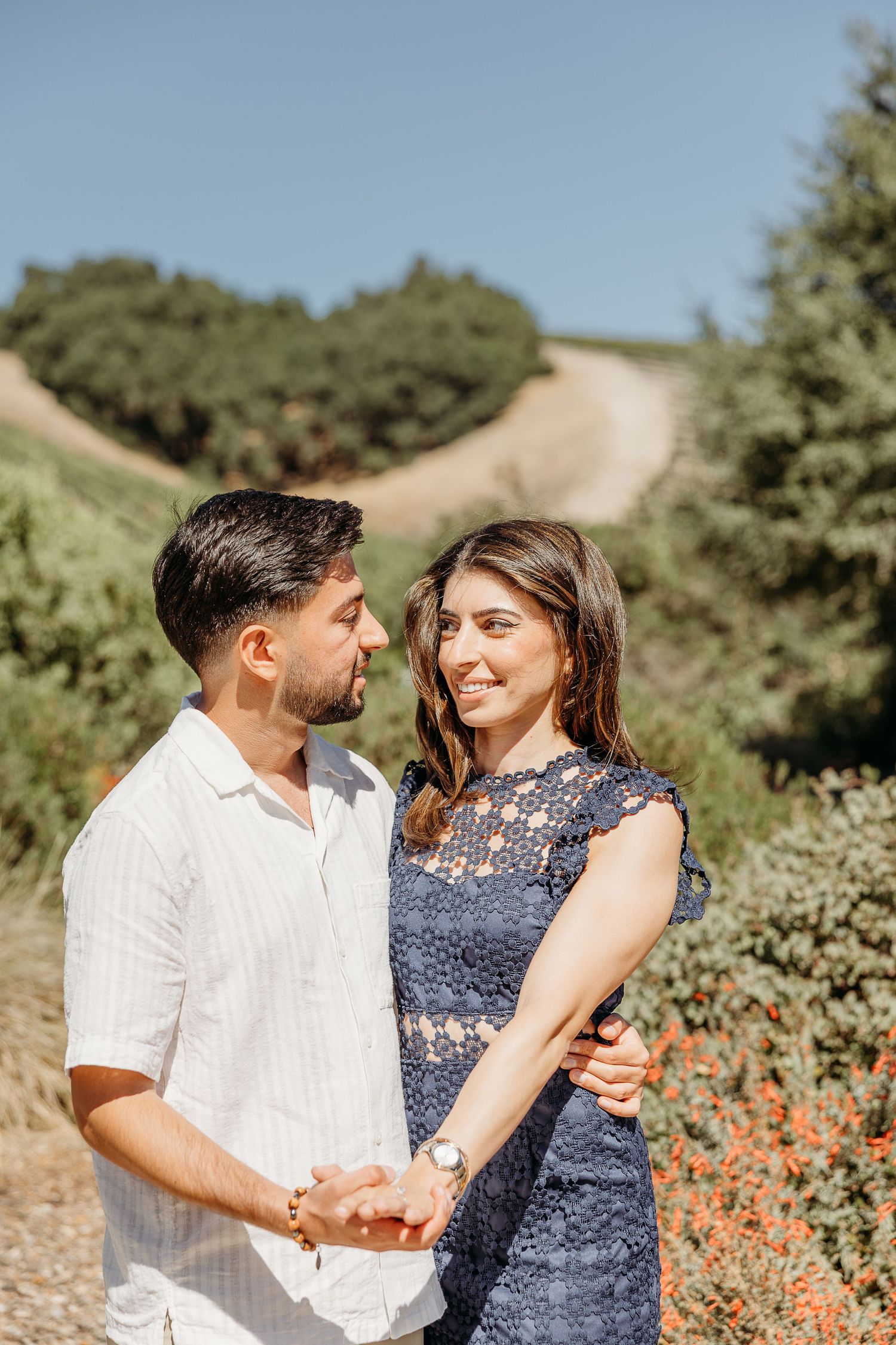 Couple shares romantic moment in outdoor field with orange wildflowers and green foliage.