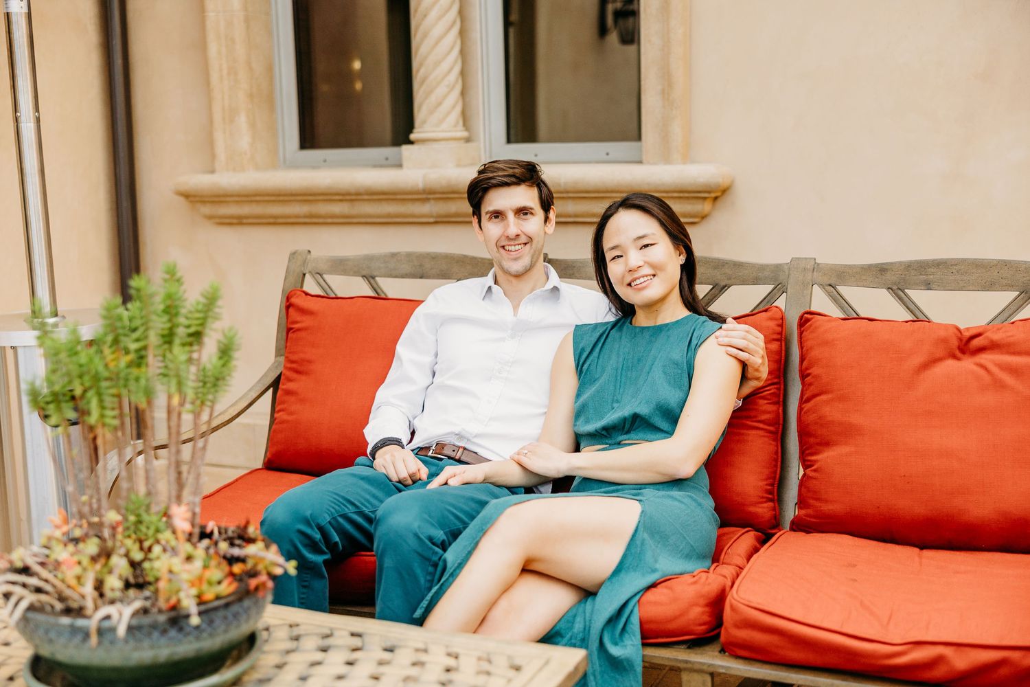 A couple relaxes together on orange outdoor cushions at an elegant patio seating area.
