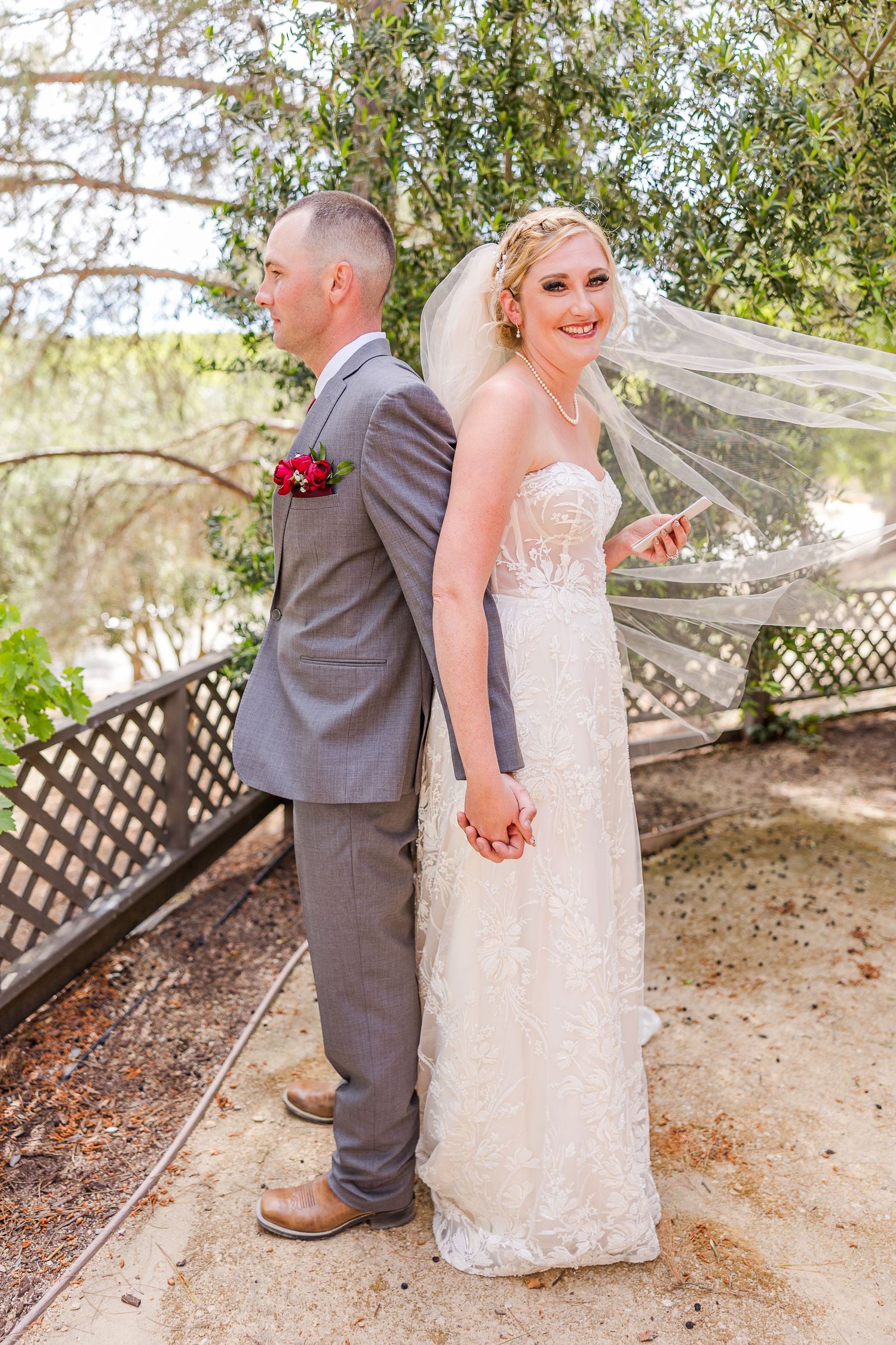 A couple in wedding attire stands back-to-back sharing a special moment on their big day.