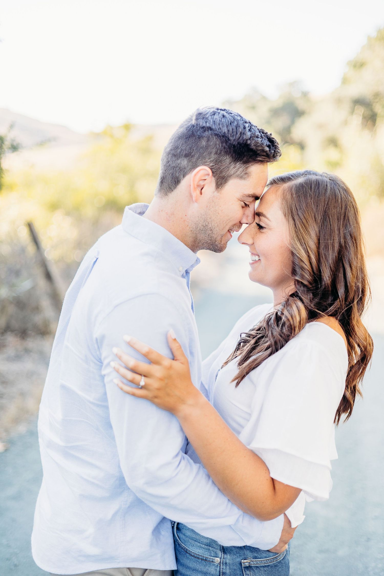 Intimate moment between couple in coordinated white and blue outfits on nature trail.