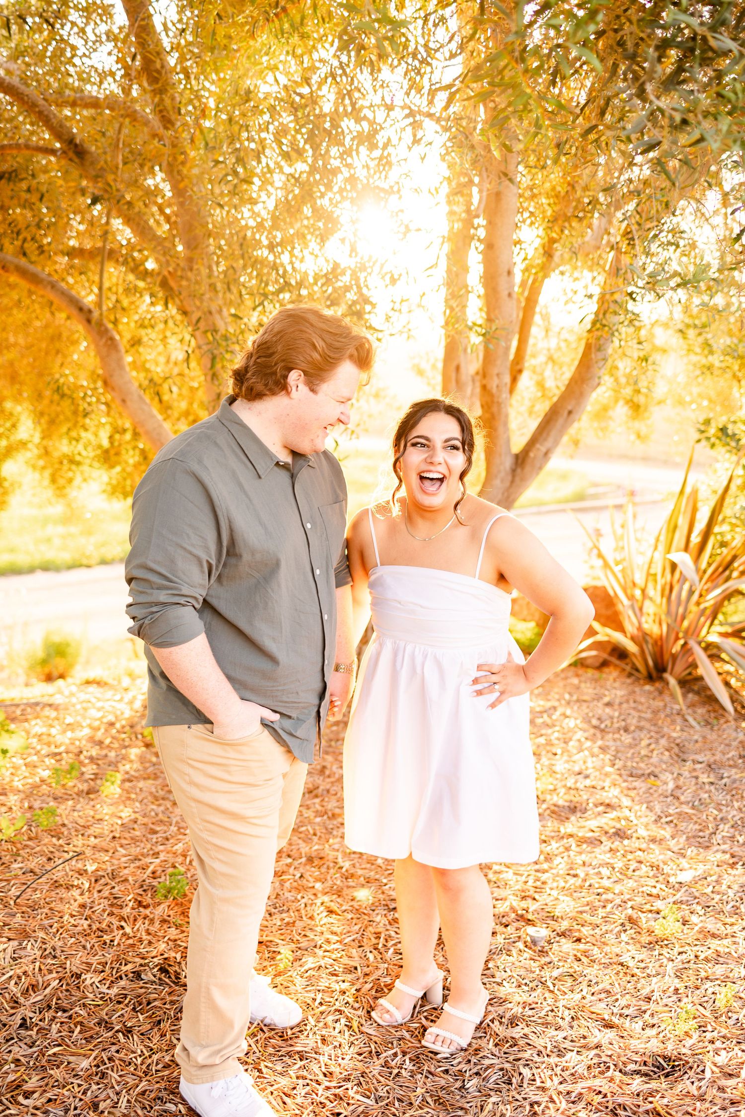 A couple laughs together during a sunset photoshoot in a garden setting.