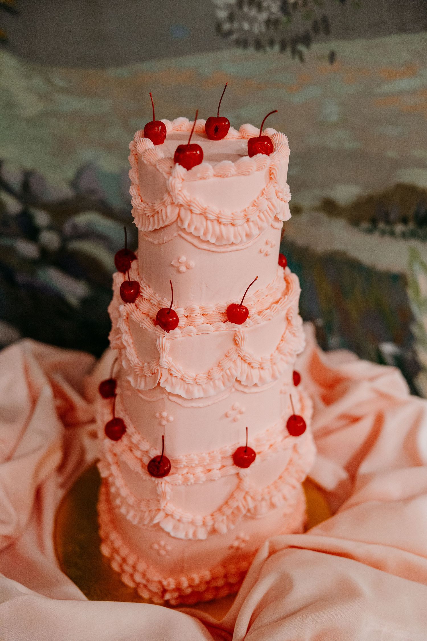 Pink tiered wedding cake decorated with delicate piping and topped with bright red cherries.