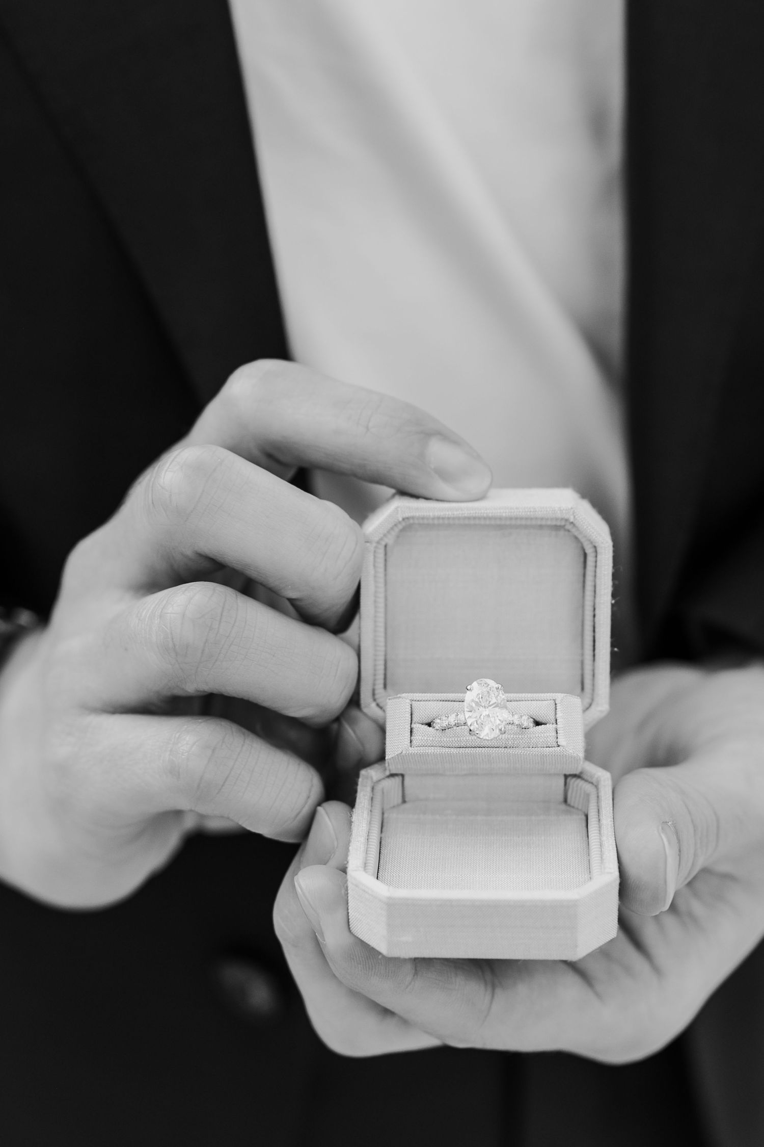 Black and white photo of hands holding an open ring box with a diamond engagement ring inside.