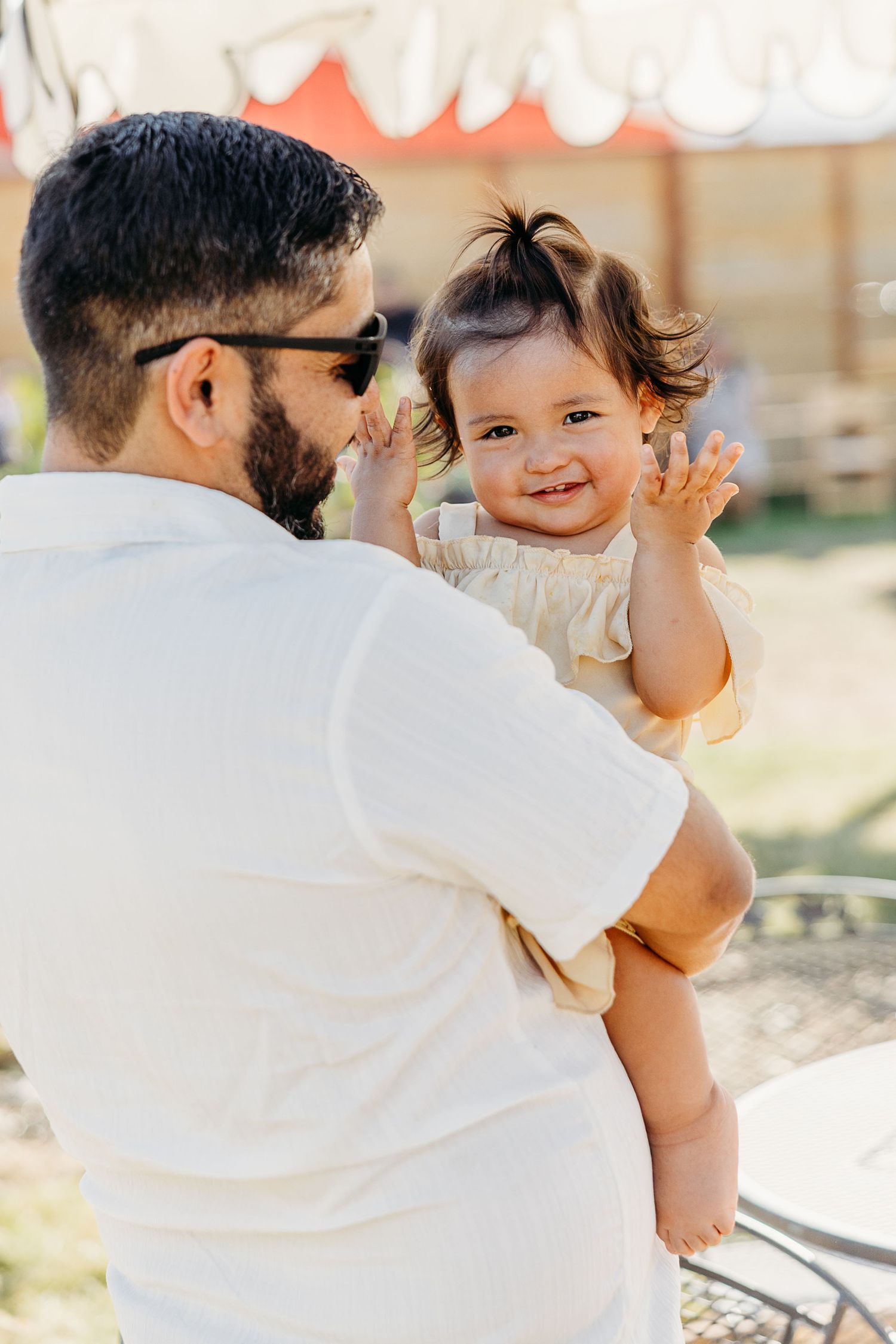 Sweet candid moments between parent and child in white attire against sunny backdrop.