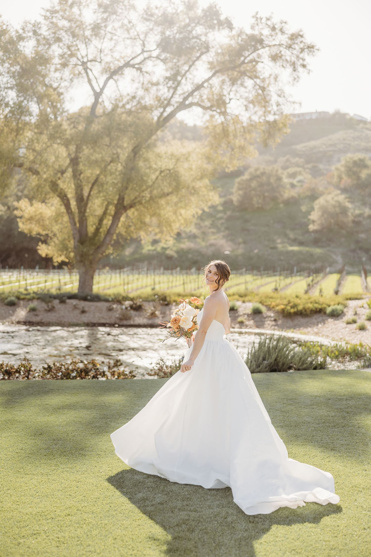 Bride in flowing white gown twirling on manicured lawn during golden hour.