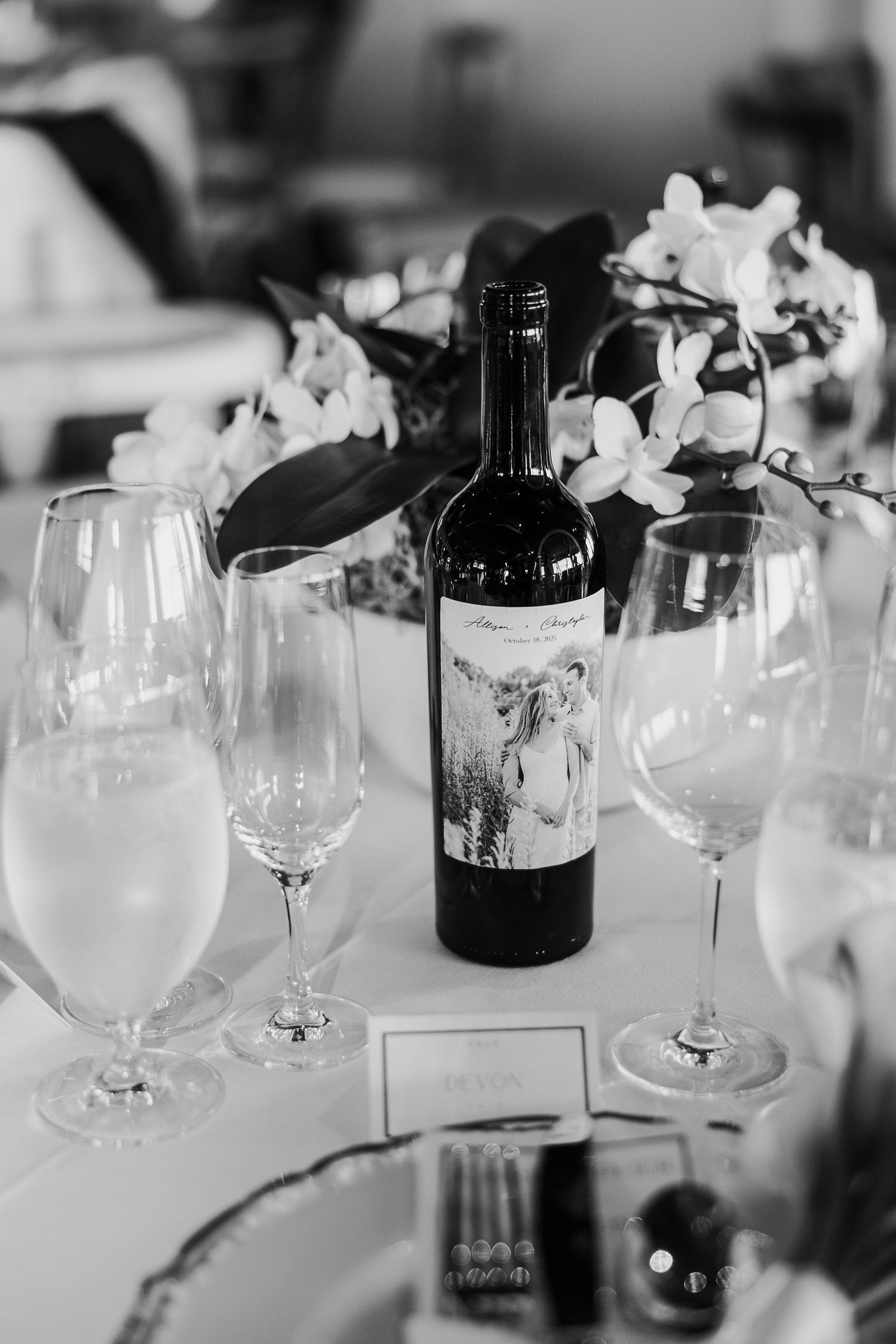 A black and white photo of wine glasses and bottle on an elegant table with orchid flowers.