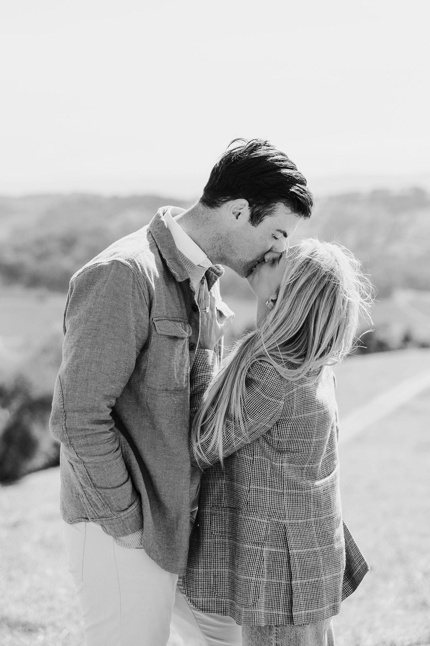 Black and white portrait of a couple sharing an intimate moment in a sunny field.