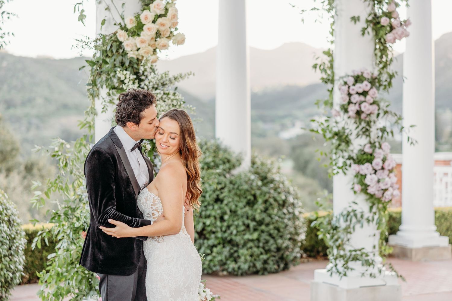 White wedding ceremony space decorated with pink floral arrangements and mountain views in the background.