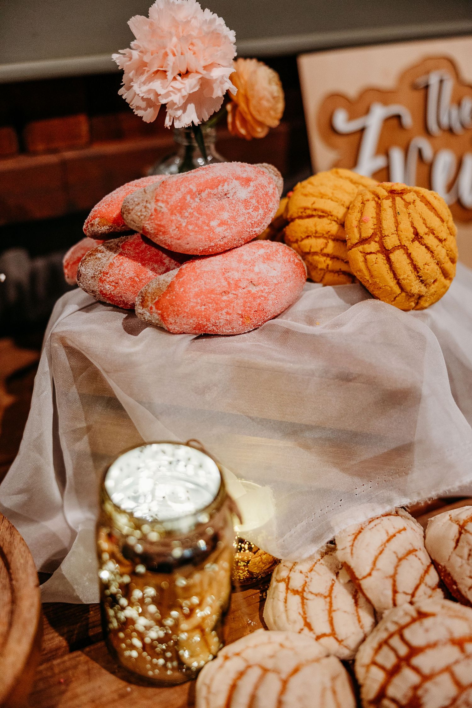 Wedding dessert table with pink cookies, golden treats and decorative mercury glass accents.