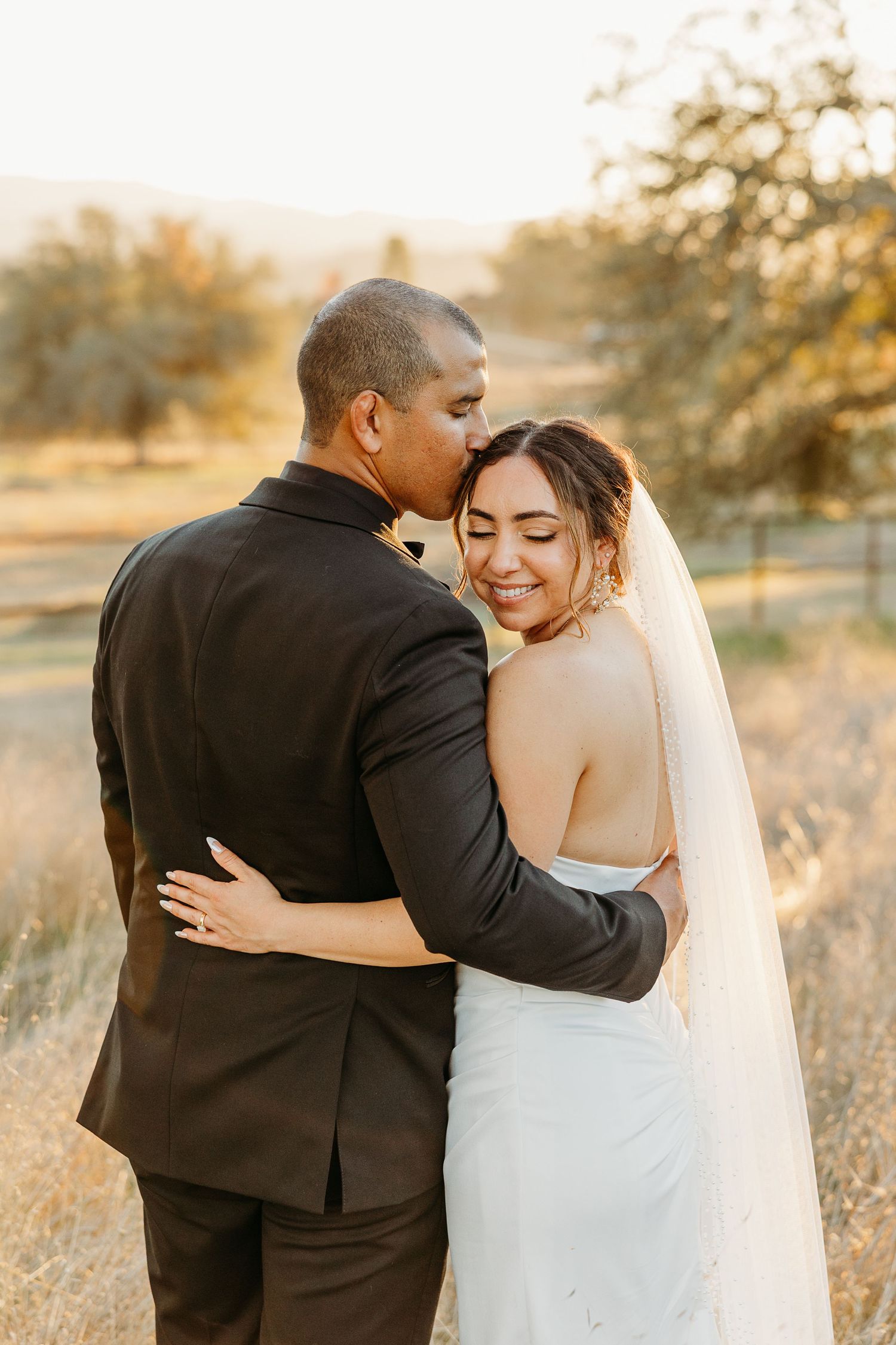 Newlyweds embrace in a golden field during sunset.