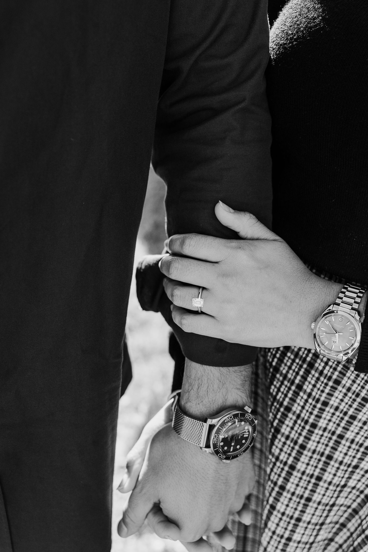 A black and white close-up of two hands with watches and rings touching affectionately.