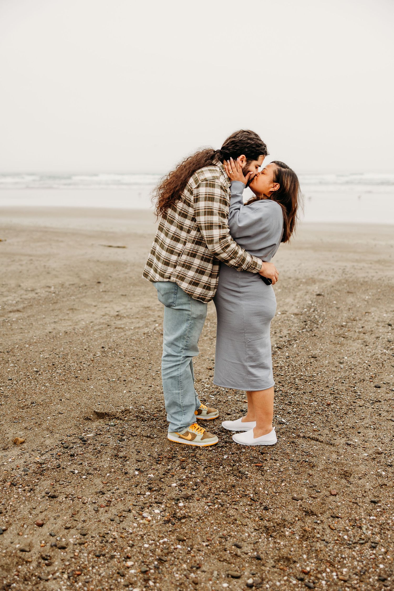 A loving couple sharing an intimate moment while embracing on a misty beach in casual attire.