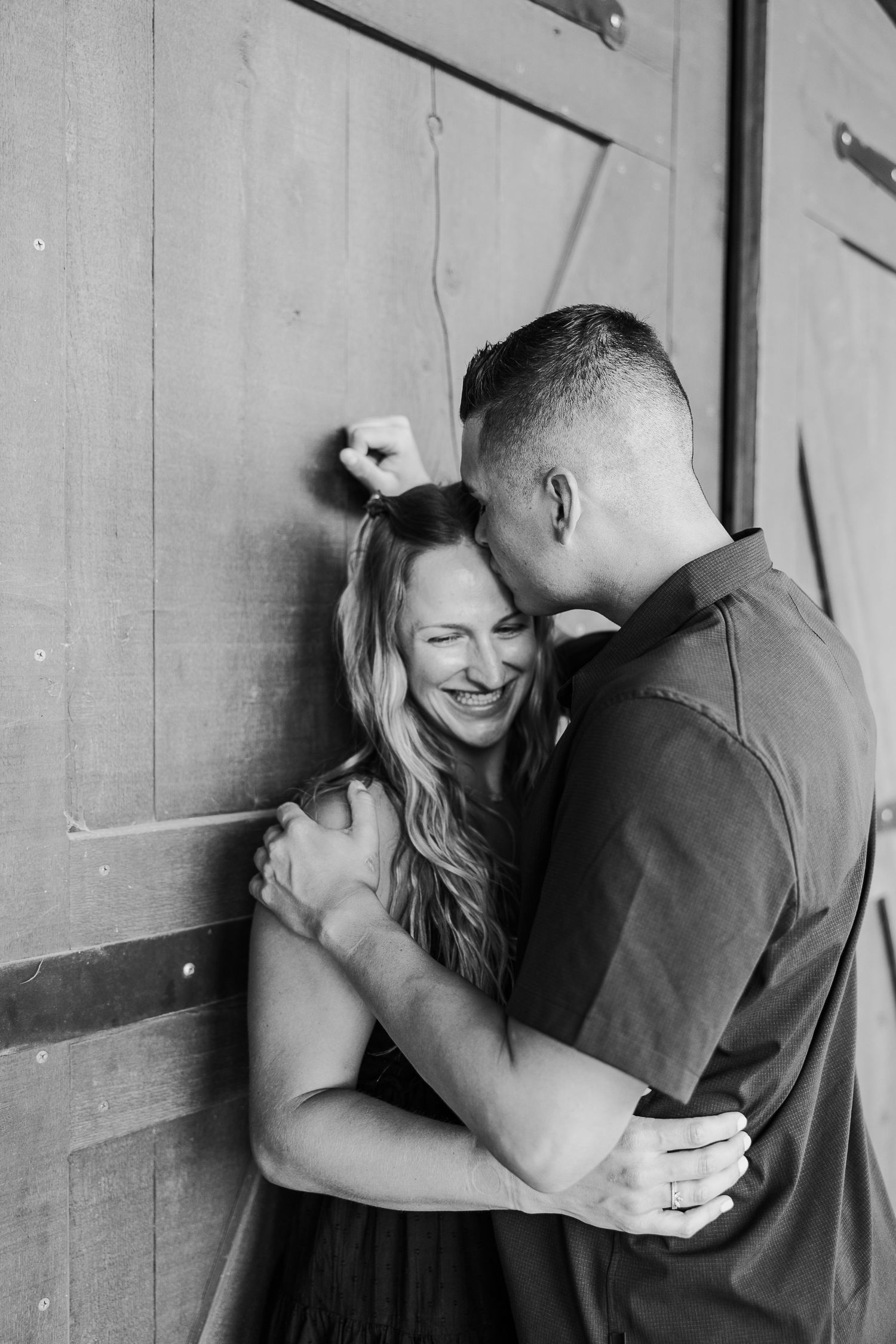 A couple shares an intimate black and white moment together against a rustic wooden door.