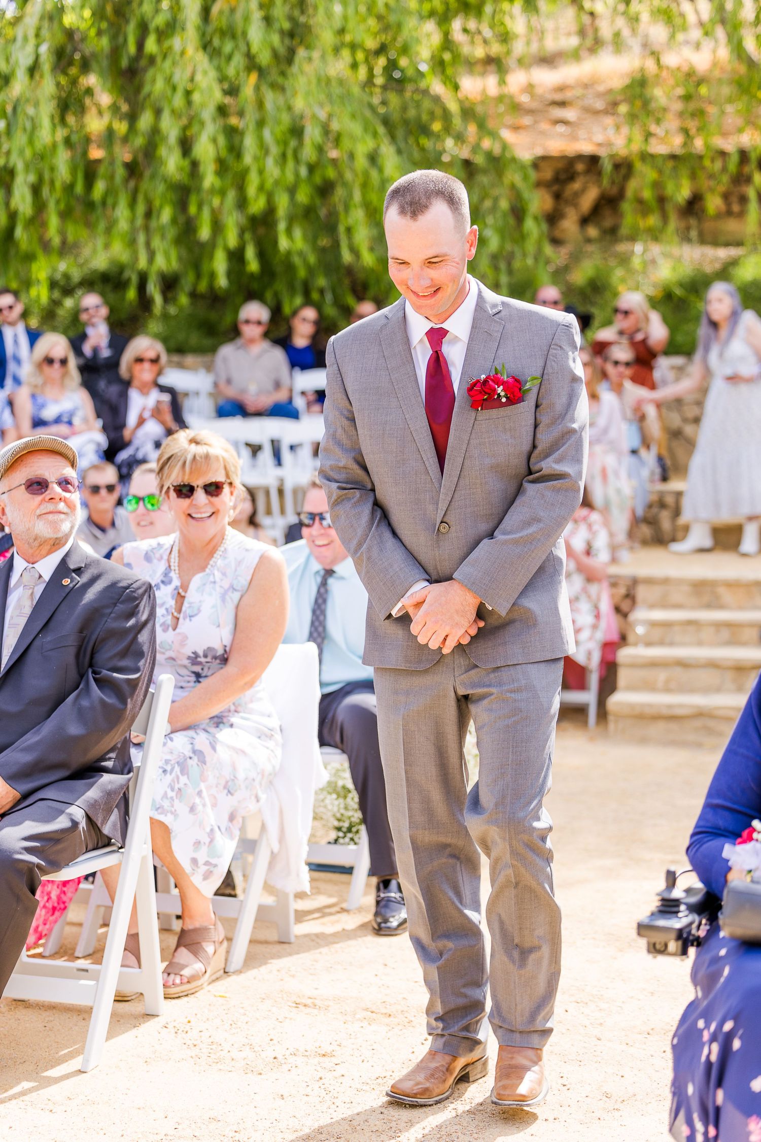 A formal gathering at an outdoor venue with stone steps and weeping willows in the background.