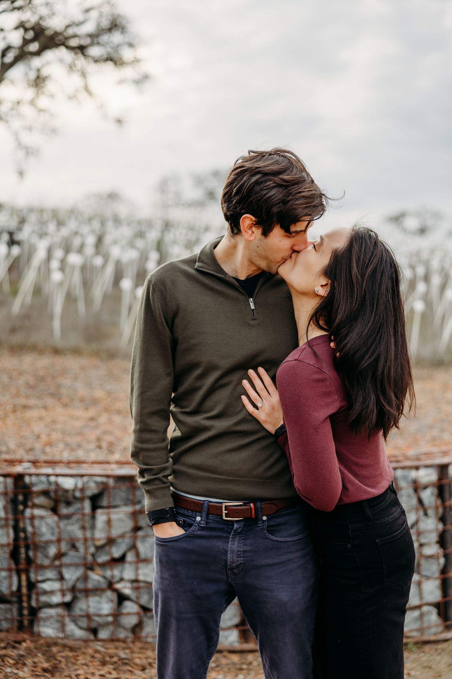 A couple sharing intimate moments in casual attire against a rustic fence and autumn backdrop.