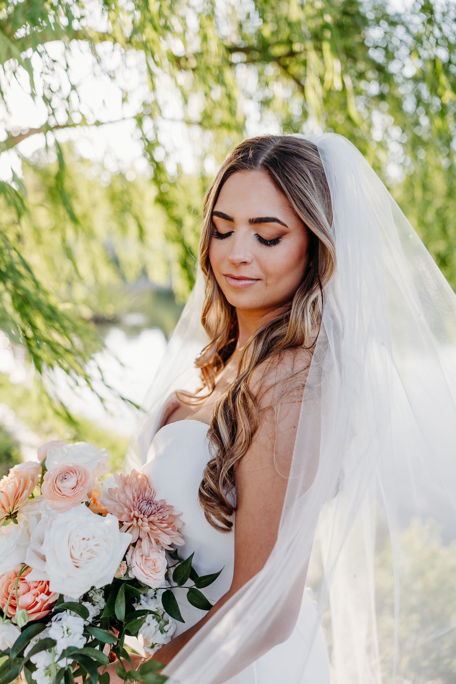 Close-up bridal portrait showcasing romantic makeup and a delicate veil against willow tree backdrop.