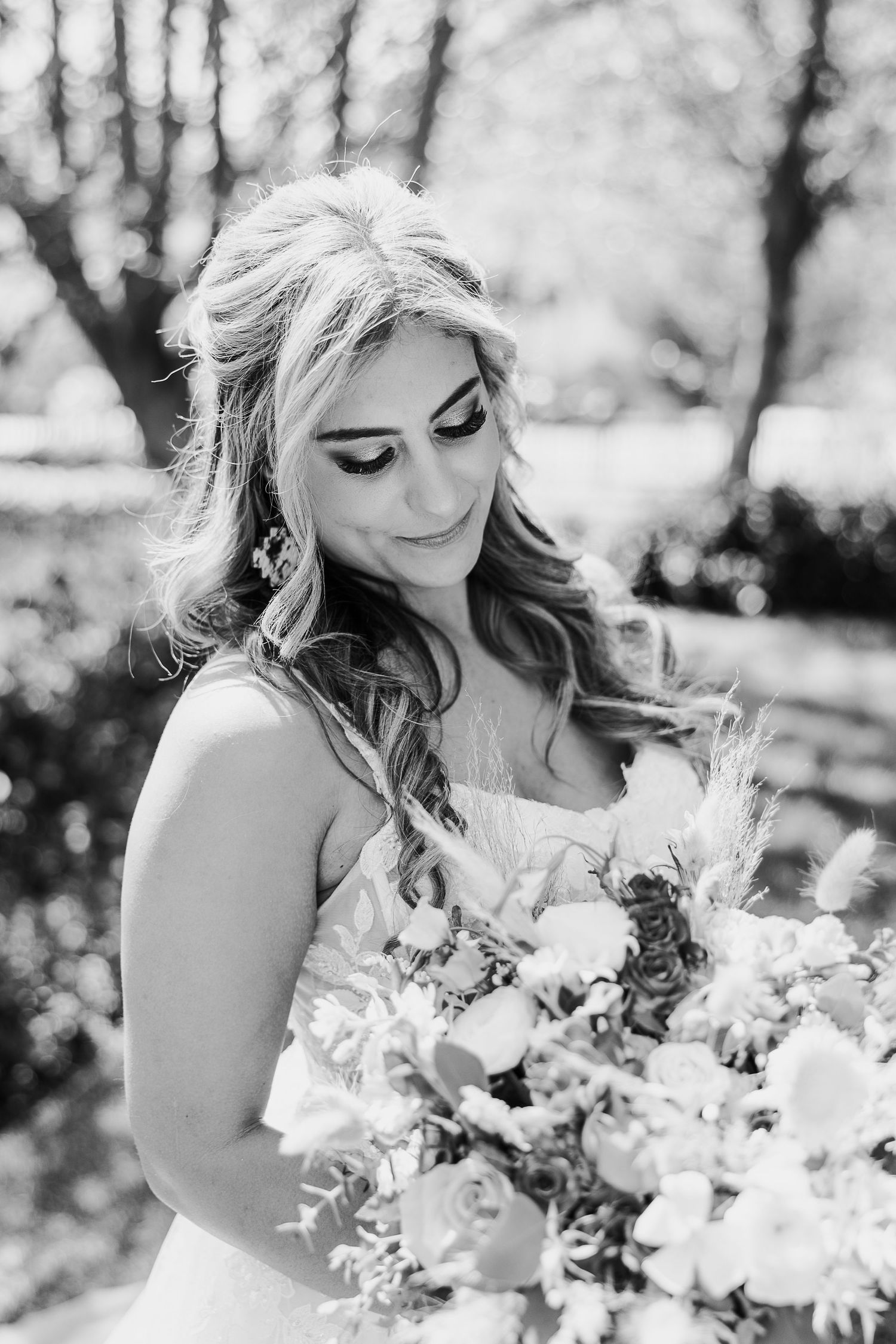 A black and white portrait of a bride looking down at her rustic floral bouquet in an outdoor setting.