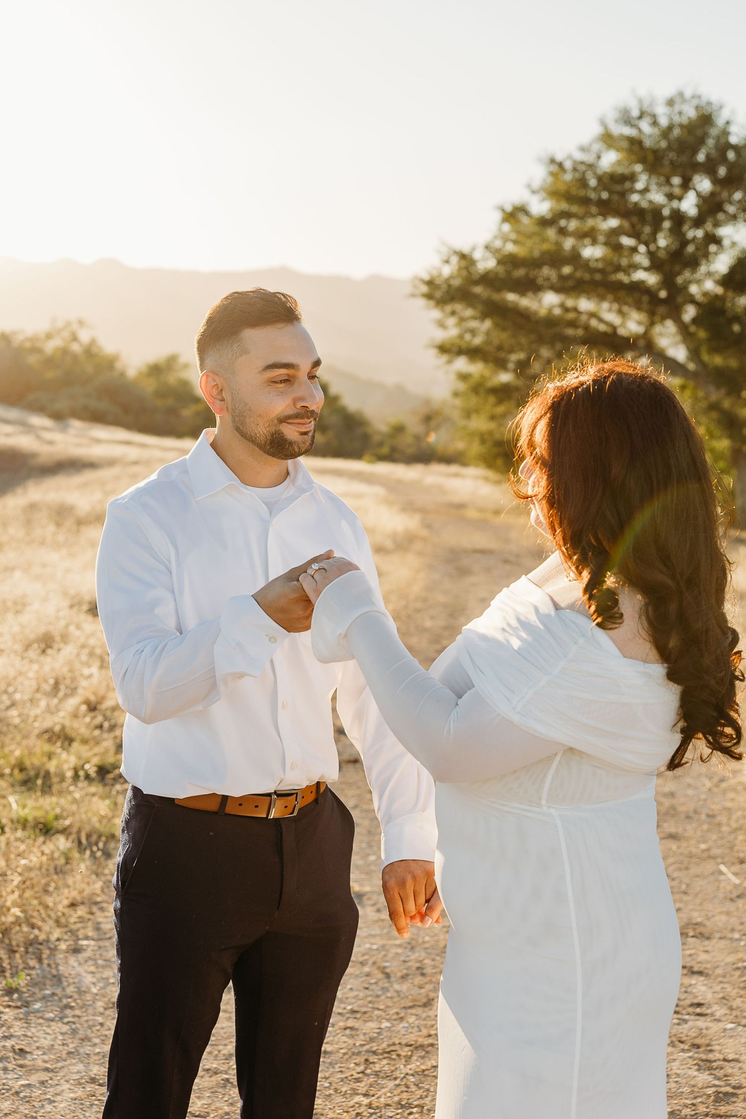 Couple dancing together in golden sunlit field wearing coordinated white and black outfits.