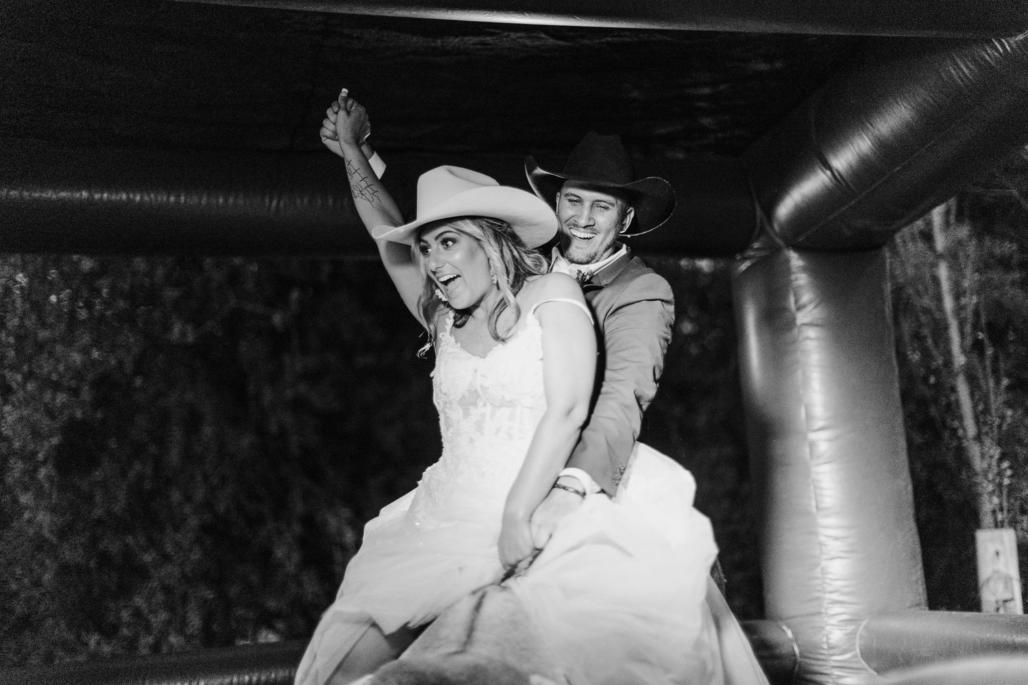 A playful wedding couple in western attire having fun on a bouncy castle.
