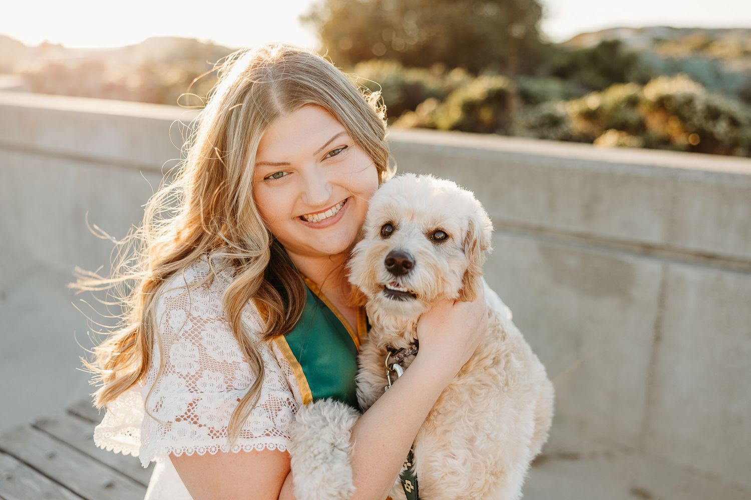 A white fluffy dog snuggles with someone in a lace dress during a golden hour photoshoot.