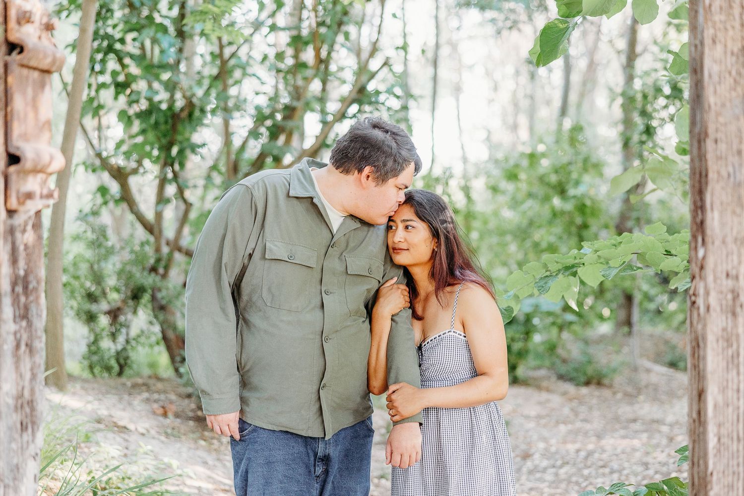 A romantic couple shares an intimate moment while walking together on a wooded trail in natural lighting.
